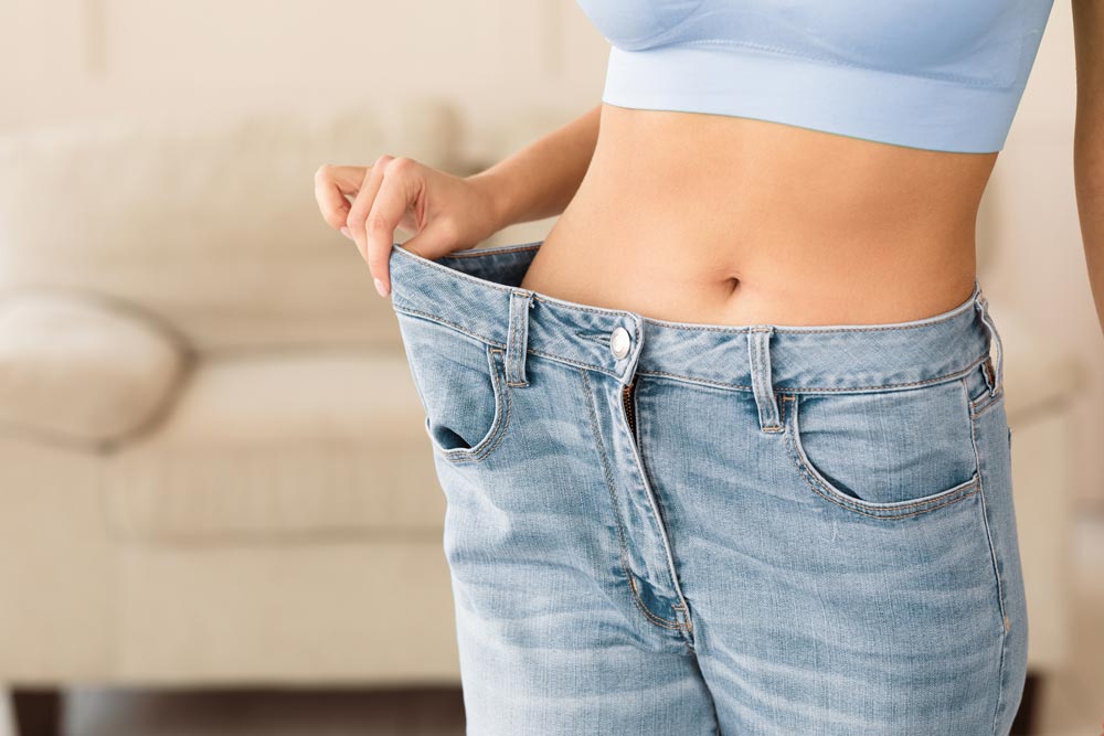 pacific-center-weight-loss - Pacific Center Plastic Surgery Person pulling the waistband of oversized jeans to show they no longer fit.